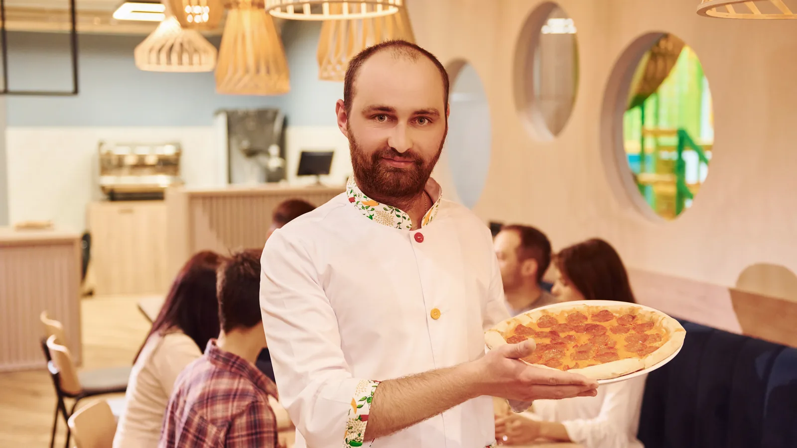 Właściciel pizzerii z pizzą w sali restauracji