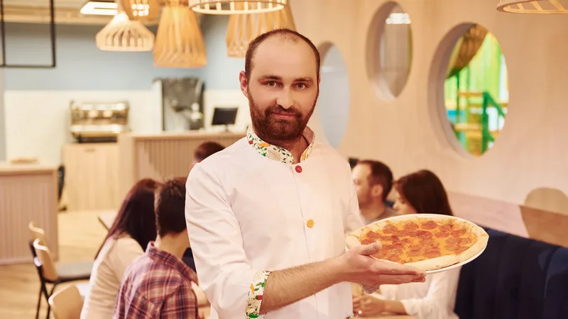 Właściciel pizzerii z pizzą w sali restauracji