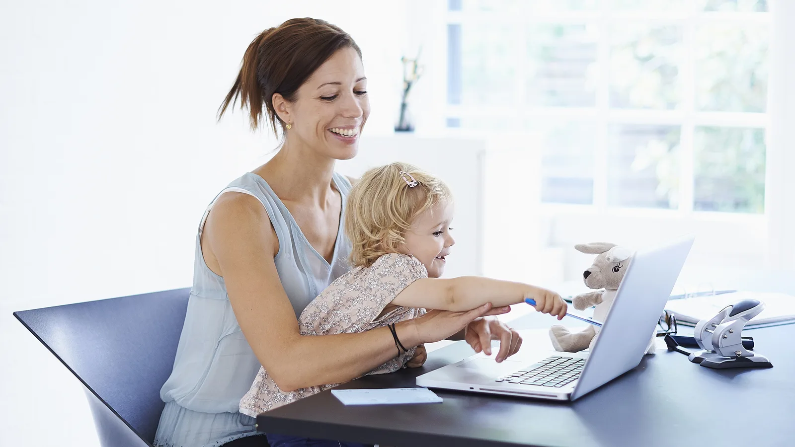 Pracownica pracuje przy laptopie w domu, obok siedzi dziecko